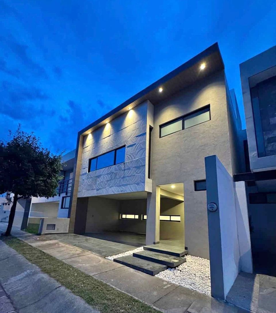 Fachada de la casa iluminada al atardecer, con el acceso y la cochera techada