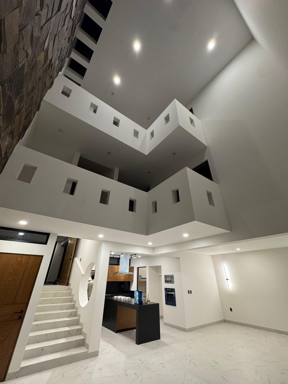 Vestíbulo de triple altura sobre la sala, con el muro de piedra natural y los dos niveles de barandal